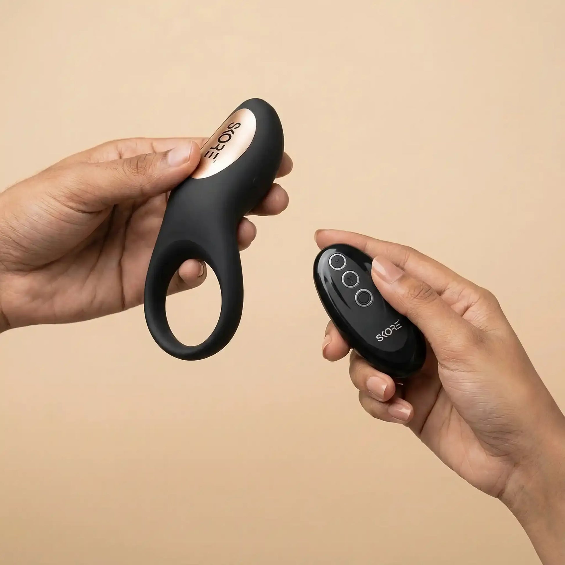 Skore Buzzz vibrating ring and remote held in hands showing the ergonomic design and gold accents.